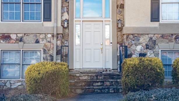 Une maison en pierre à deux étages, avec une porte d’entrée blanche, des murs en pierre et un petit porche à l’avant.