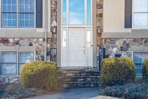 A two-story stone house with a white front door, stone walls, and a small front porch. - Cartersville Home with Basement Media Room & Yard (Cartersville)