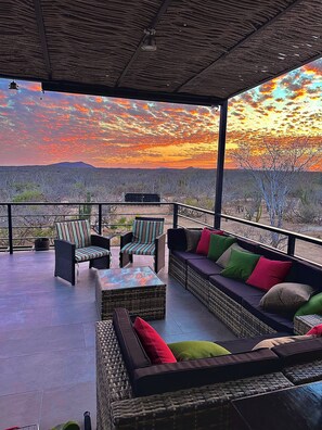 Uma área externa com mobiliário de vime e vista para a paisagem desértica ao pôr do sol.