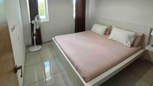 Ein Schlafzimmer mit einem Bett, einem Standventilator und einem Fenster mit Vorhängen.