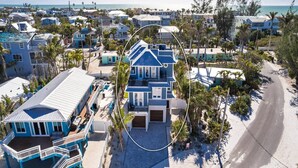 A beachfront property with a large house featuring a balcony and a covered patio. - Salt Dreams: 1 Block to Beach! Pool, Spa, Games, Rooftop Deck by Anna Maria Life Vacation Rentals (Anna Maria)