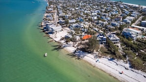 An aerial view of a coastal residential area with houses, a beach, and a clear blue sky. - Salt Dreams: 1 Block to Beach! Pool, Spa, Games, Rooftop Deck by Anna Maria Life Vacation Rentals (Anna Maria)