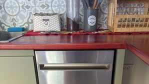 Un lavavajillas de acero inoxidable en una cocina con encimera roja, un jabonera de patrón hexagonal y un caja de madera con diseño de bigote negro.