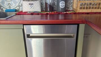 A stainless steel dishwasher in a kitchen with a red countertop, a hexagonal patterned soap dish, and a wooden crate with a black mustache design.