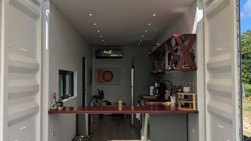 A compact, open container with a kitchenette, two stools, and a small dining area.