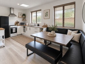 A modern kitchen with a black refrigerator, stove, and oven, wooden countertops, and a dining area with a bench and a table.
