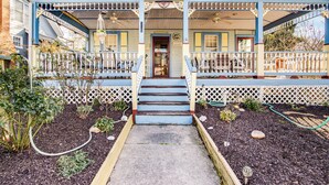 Una casa de dos pisos con un porche, una puerta principal y un pequeño jardín con mantillo y plantas.