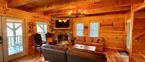 A cozy cabin interior with a stone fireplace, wooden walls, a sofa, and a television mounted above it.