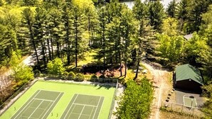Ein Tennisplatz, umgeben von dichtem Wald und einem See.