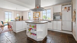 A modern kitchen with white cabinetry, a central island with storage baskets, a stainless steel range hood, and a large window providing natural light. - 2 bedroom nice home in Hemmet (Hemmet)
