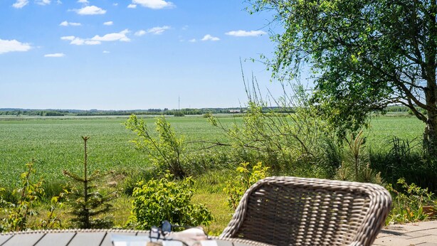 A wicker chair with a newspaper on a wooden table, overlooking a green field and a clear sky. - 2 bedroom nice home in Hemmet (Hemmet)