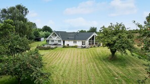 Une maison blanche avec un toit en pente, entourée d’une pelouse bien entretenue et d’arbres.