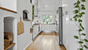 Une cuisine étroite avec des meubles blancs, un plancher en bois et une fenêtre donnant sur un paysage verdoyant.