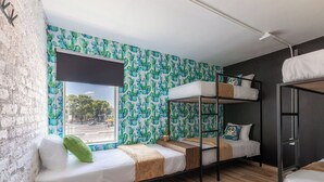 Une chambre de type dortoir avec des lits superposés, une fenêtre donnant sur la rue et un mur décoré de motifs de cactus.