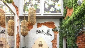 Un jardin intérieur accueillant, avec un mur de briques rustiques, un banc en bois, des guirlandes lumineuses en osier suspendues et une fontaine.