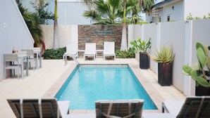 A swimming pool with lounge chairs and a brick wall with text. - Palapa Suite # 7, walk to Eagle Beach (Eagle)