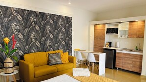 A modern hotel room with a yellow sofa, a bed with white bedding, a dining area with a white table and chairs, and a kitchen with wooden cabinets. - Palapa Suite # 7, walk to Eagle Beach (Eagle)