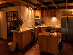 A kitchen with wooden cabinets, a microwave, a refrigerator, a sink, and a dining area with two wine glasses and candles.