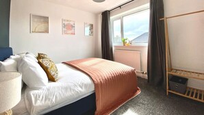 Ein Hotelzimmer mit Bett, einem Fenster mit Vorhängen, einem Nachttisch und einem Wandregal.