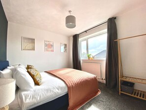 Ein Hotelzimmer mit Bett, einem Fenster mit Vorhängen, einem Nachttisch und einem Wandregal.
