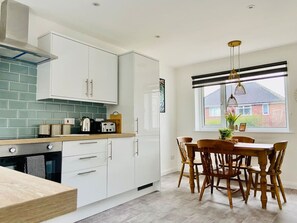 Una cocina moderna con armarios blancos, una encimera de madera y un comedor con mesa y sillas.
