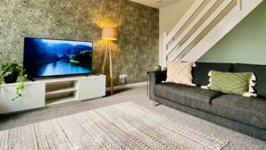 Ein modernes Wohnzimmer mit Flachbildfernseher, Stehlampe, dunklem Sofa und Treppe.