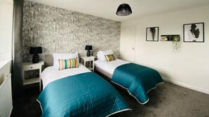 Ein Hotelzimmer mit zwei Betten, einem gemusterten Wandpapier, einer schwarzen Pendelleuchte und gerahmten Bildern an der Wand.