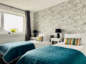 Habitación de hotel con dos camas, una ventana con cortinas, un radiador y una pared con diseño de árbol.