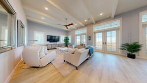 A spacious living room with a large TV, comfortable seating, and a balcony with a view. - Sea View, Shared Resort Style Pools, Boardwalk to the Beach, Golf Cart Access (Port Aransas)