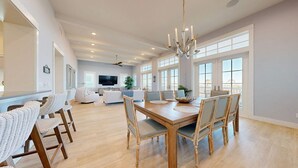A spacious living area with a dining table, chairs, and a chandelier. - Sea View, Shared Resort Style Pools, Boardwalk to the Beach, Golf Cart Access (Port Aransas)