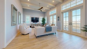 A spacious living room with a large TV, comfortable seating, and a view through the glass doors. - Sea View, Shared Resort Style Pools, Boardwalk to the Beach, Golf Cart Access (Port Aransas)