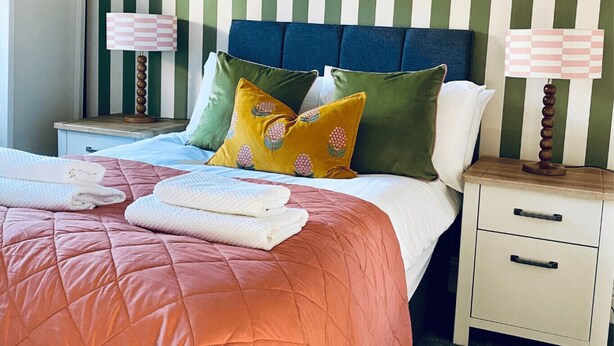 A neatly made bed with a pink quilt, two pillows, and folded towels on a nightstand. - Halifax Centre → 8 min | Dogs OK | 50”TV | Parking (Halifax)