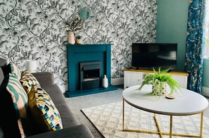 A living room with a fireplace, sofa, television, and decorative plants.