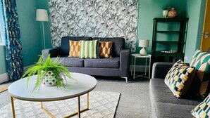 A living room with a grey sofa, patterned cushions, a round coffee table with a plant, and a green bookshelf. - Halifax Centre → 8 min | Dogs OK | 50”TV | Parking (Halifax)