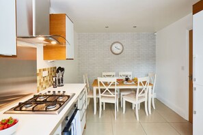 A modern kitchen with a gas stove, white cabinets, and a dining area with white chairs.