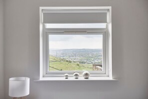 A room with a window overlooking a green landscape and a city view.
