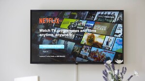 Een flatscreen-televisie aan de muur met een Netflix-interface en verschillende thumbnails van tv-series en films.