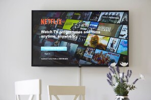 Een flatscreen-televisie aan de muur met een Netflix-interface en verschillende thumbnails van tv-series en films.