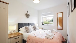 Een slaapkamer met een bed, nachtkastje, lamp en een raam met uitzicht.