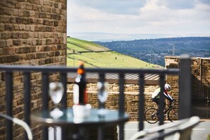 Une vue depuis un balcon, avec un mur en pierre et un cycliste aperçu au loin.