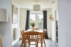 Een eetgedeelte met een houten tafel en stoelen, een potplant en een hanglamp.