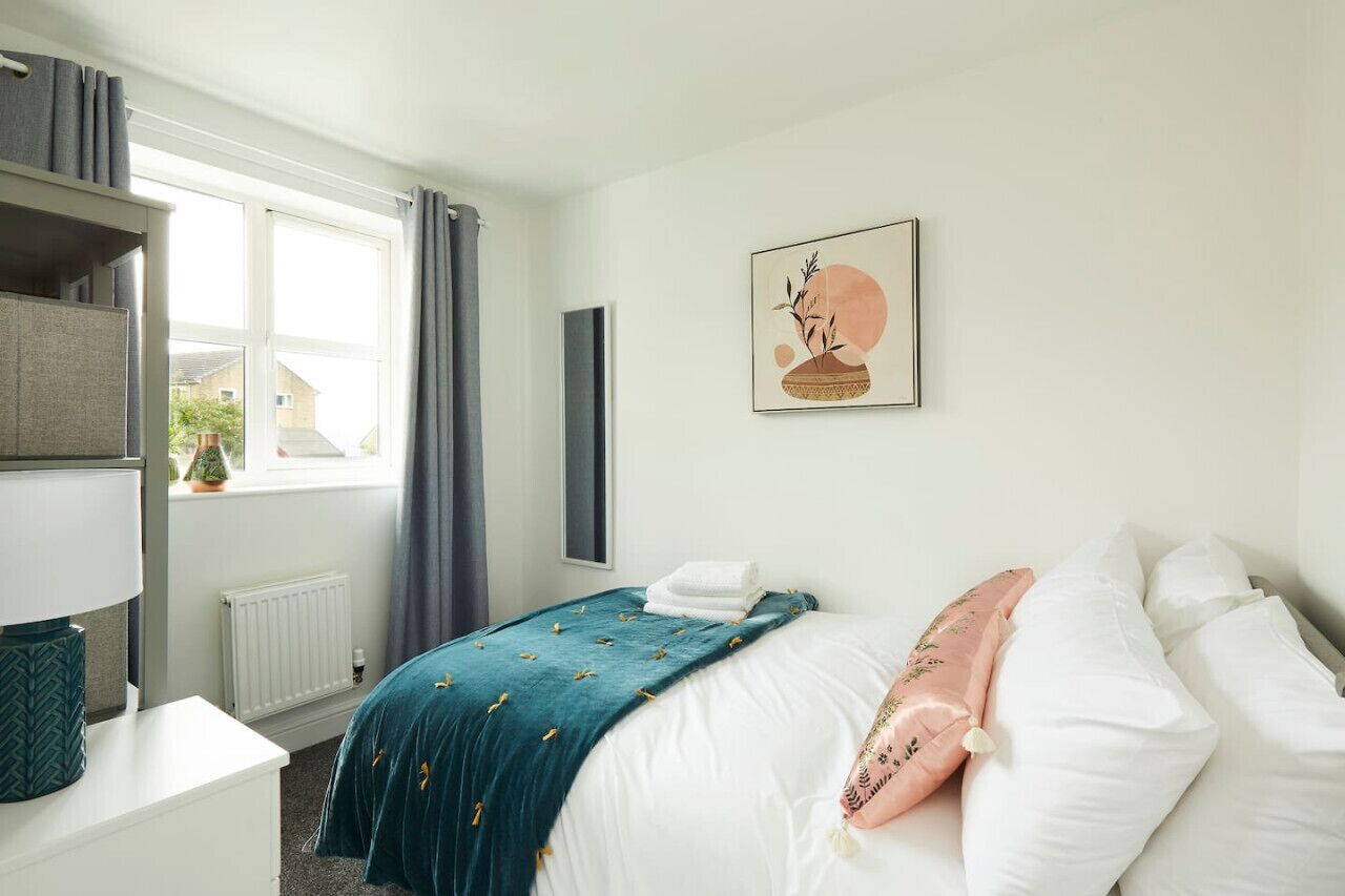 Une chambre à coucher comprenant un lit, une table de chevet, une fenêtre avec des rideaux, un radiateur et une œuvre d’art accrochée au mur.