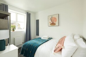 Een slaapkamer met een bed, nachtkastje, raam met gordijnen, verwarming en een wanddecoratie.