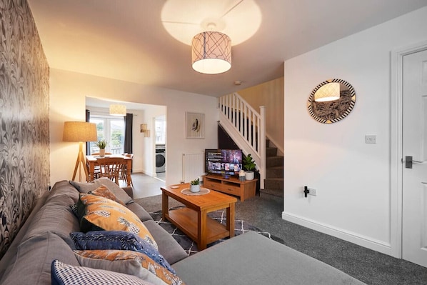 Una sala de estar con sofá, mesa de centro, televisión y una escalera que lleva a otra habitación.