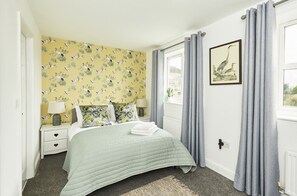 Een slaapkamer met een bed, nachtkastjes, een lamp, een raam met gordijnen en een wand met een vogelmotief.