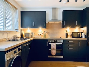 A modern kitchen with dark cabinetry, a built-in oven, a microwave, and a washing machine.