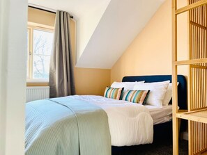 Une chambre à coucher avec un lit, une fenêtre avec des rideaux, un radiateur et un plafond en pente.