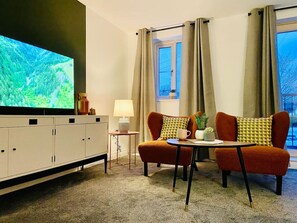 A room with a TV, a sofa, a small table, a lamp, and a window with curtains.