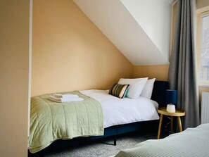 A bedroom with a bed, pillows, a bedside table with a lamp, and a window with curtains.