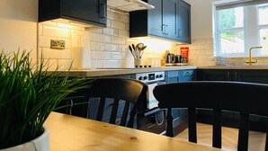 Une cuisine moderne avec des meubles de couleur sombre, un pare-feu en carreaux blancs et une table à manger en bois accompagnée de deux chaises.